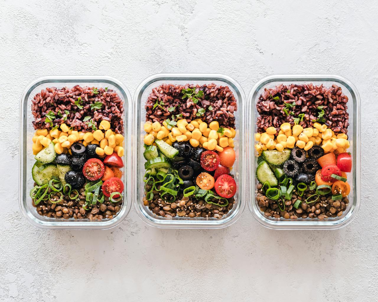 Colorful healthy meal prep with corn, olives, tomatoes, and lentils in glass containers. Perfect for mindful eating.