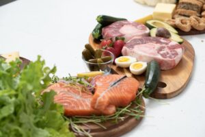 Assorted fresh keto ingredients including salmon, beef, and vegetables on wooden boards, perfect for healthy meals.